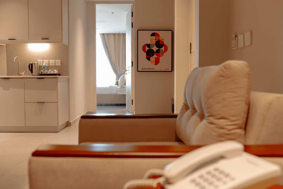 Living area with a kitchenette and a doorway into the bedroom at Cyrus One, showing the apartment-style layout of the suite in Islamabad.