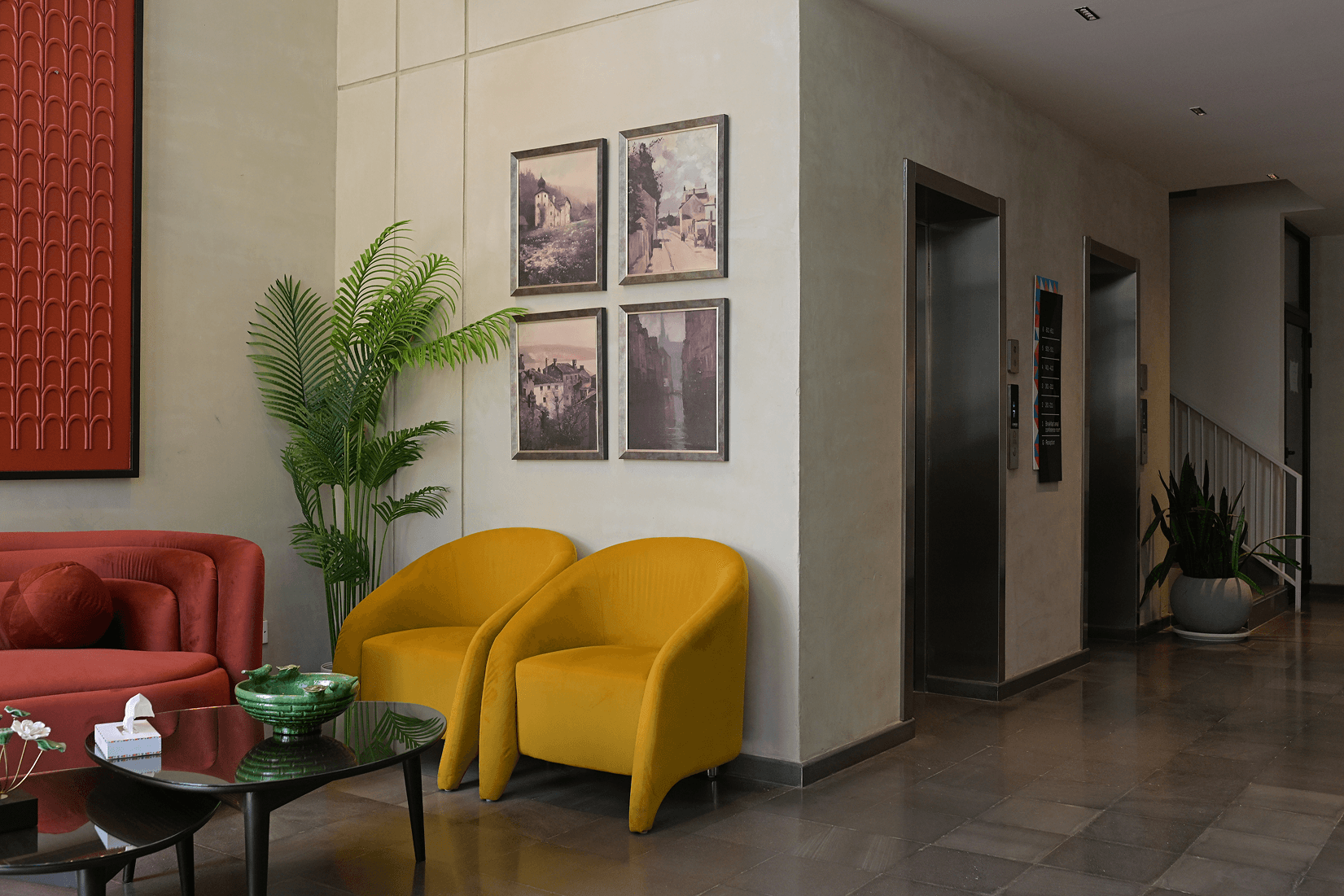 Cyrus One hotel lobby with a red velvet sofa, mustard-yellow armchairs, framed wall art, and elevator doors