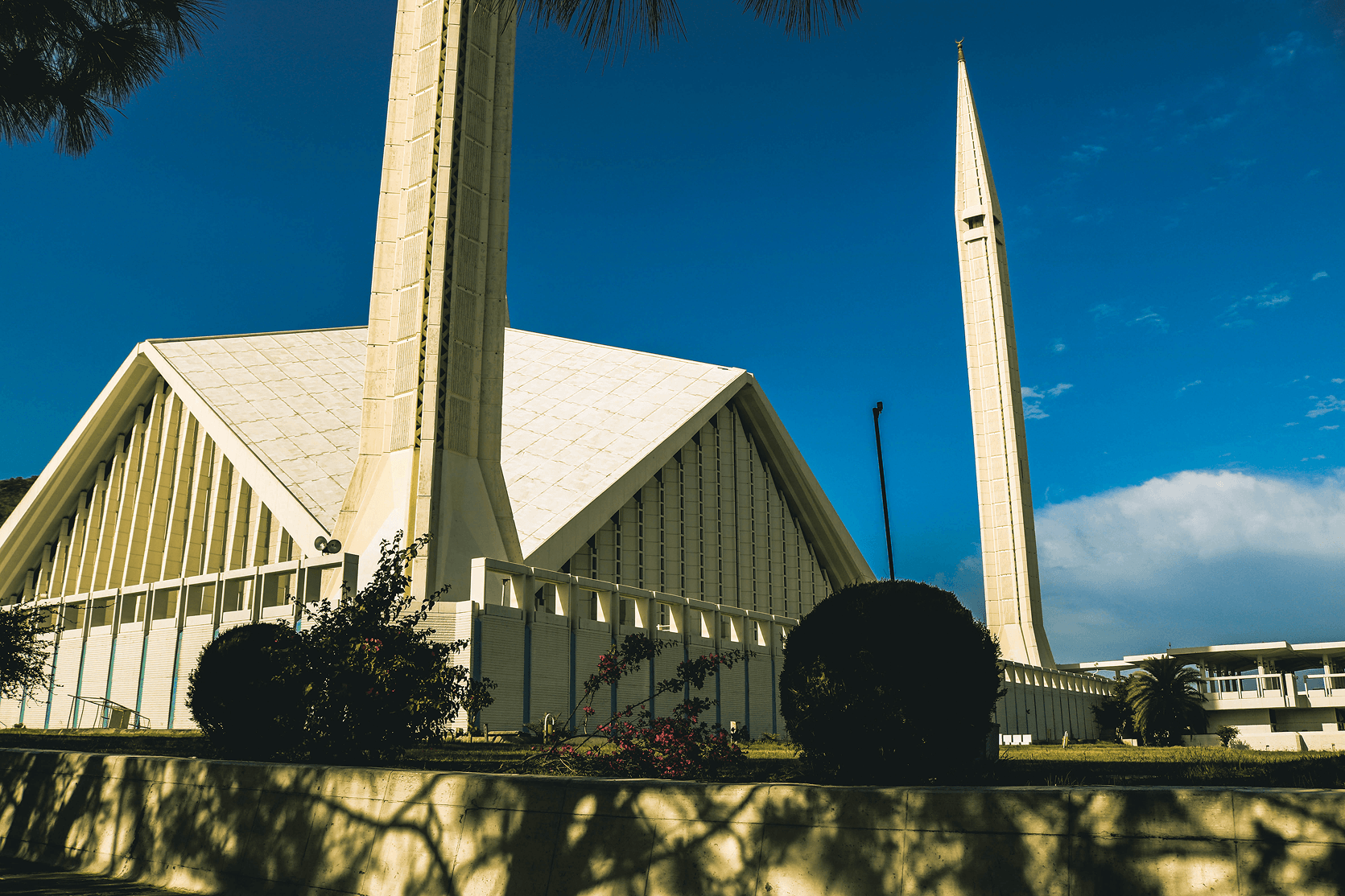 Faisal Mosque in Islamabad, showing its distinctive triangular roof and towering minarets against a clear blue sky
