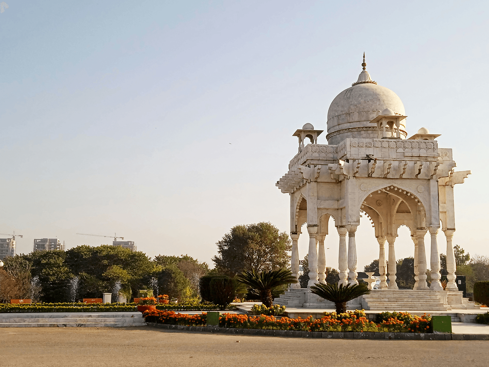 White marble domed pavilion surrounded by orange marigold flower beds and palm trees in an Islamabad F9 park